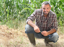 Farmer kneeling in field, happy about IL Ag Invest program