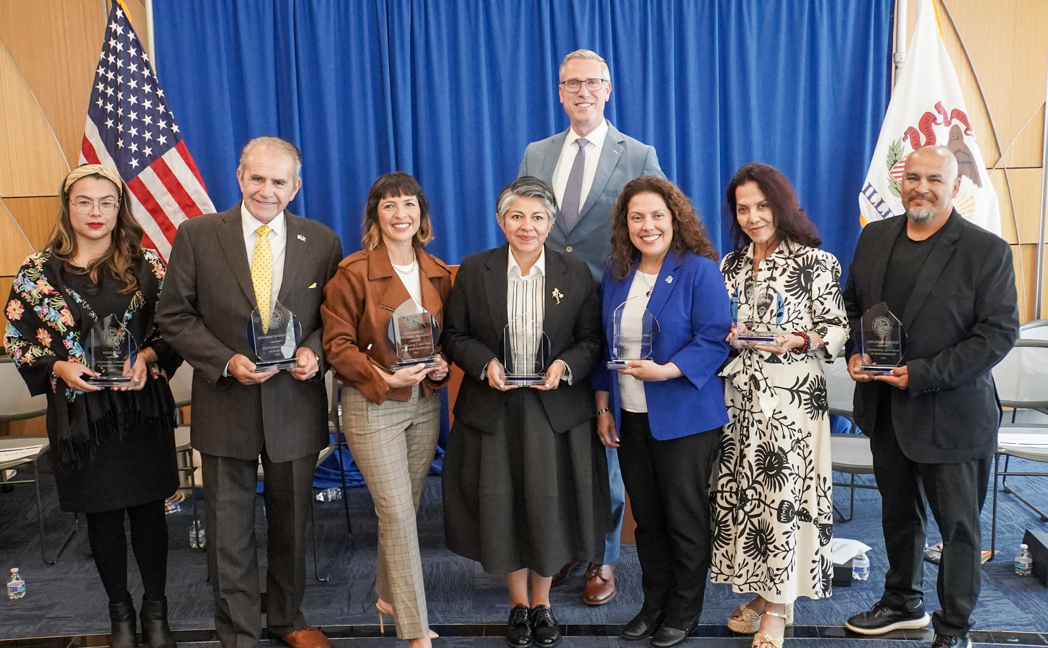 Treasurer Frerichs posing against a blue curtain and the U.S. flag with recipients of Hispanic Heritage Month awards in 2025