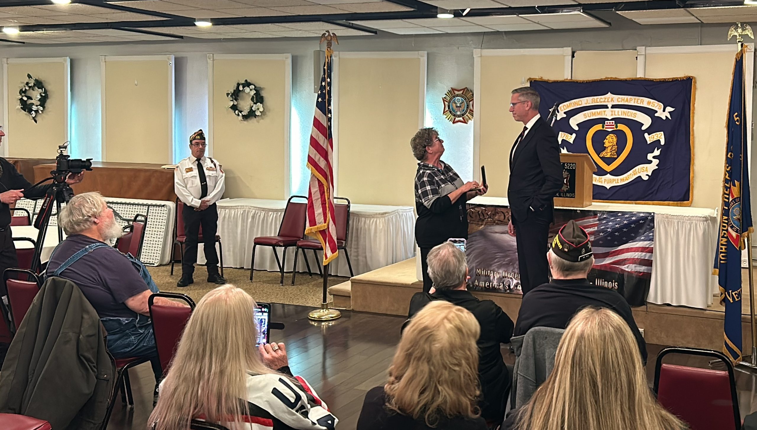 A group of people watch as Treasurer Frerichs presents a Purple Heart to Patty Knies, whose late uncle earned it