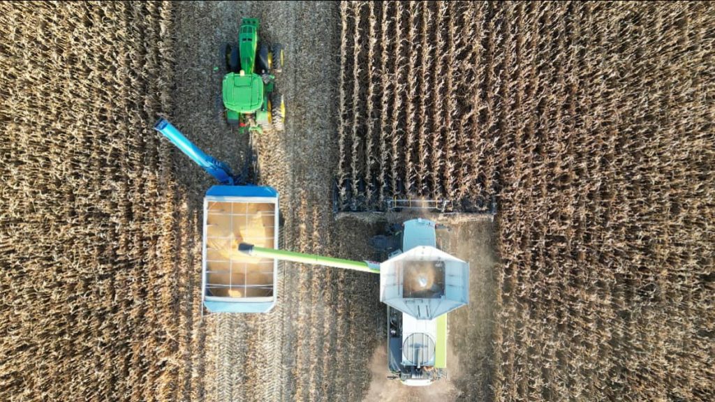 a combine farm machine harvests grain and outputs the finished product in a waiting truck pulled by a tractor