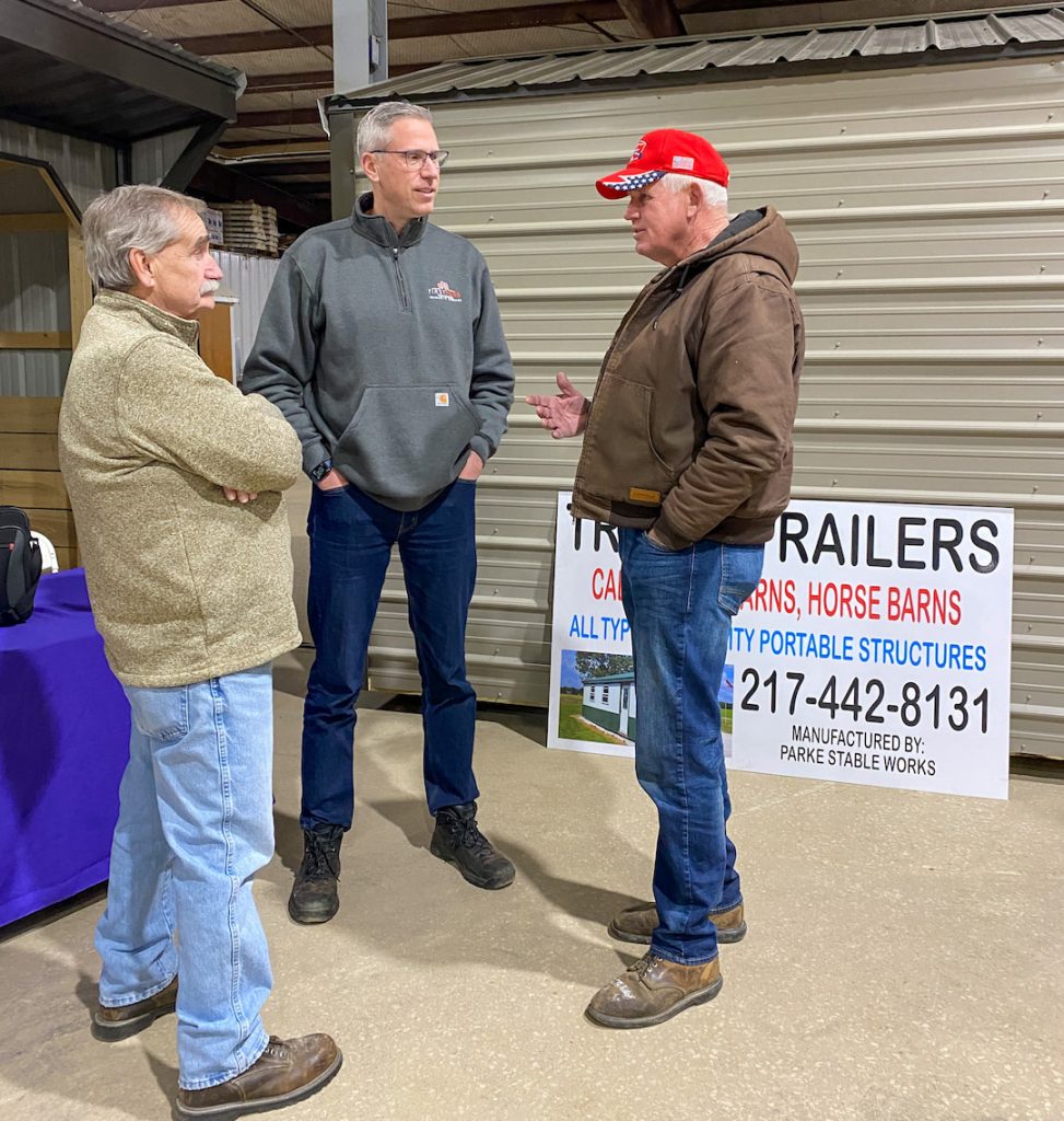three men standing having a conversation in an exposition fairground