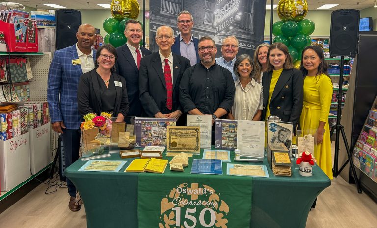 Treasurer Frerichs stands with employees of Oswald's Pharmacy at its 150th anniversary celebration