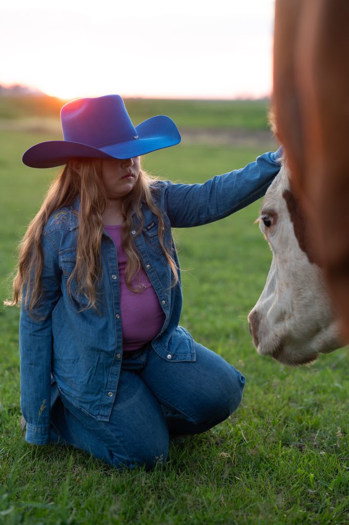 a girl wearing a cowboy hat petting a cow on its head