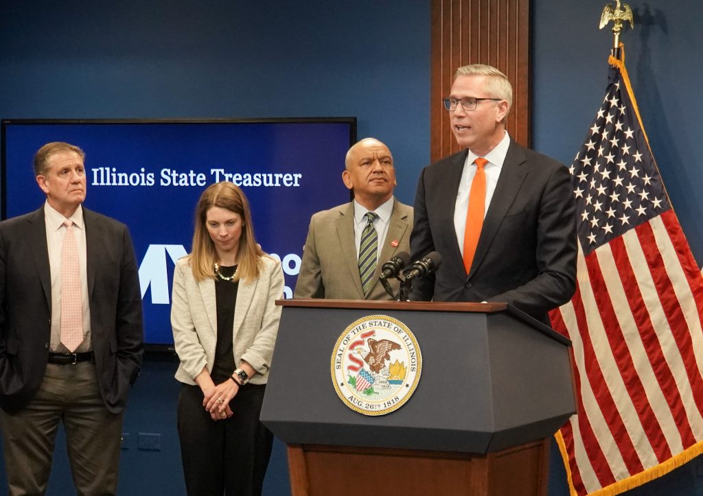 Treasurer Frerichs speaking at podium as two men and a woman stand beside him